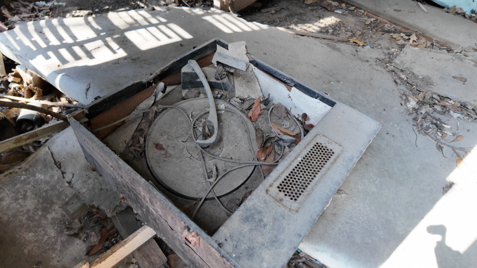 A dusty phonograph record player lies on the floor of an abandoned house